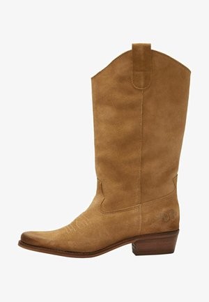 Bruine suède cowboylaars met een hoge schacht, puntige neus en subtiele witte stiksels. Bevat een gemusterde accent nabij de hak en een gestapelde houten hak.