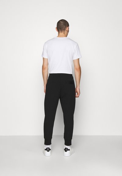 Zwarte sweatpants met geribbelde boorden, zijzakken en een achterzak. Gemaakt met een eenvoudig wit T-shirt en witte sneakers.