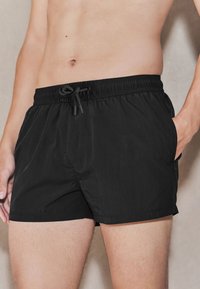 Mustad ujumispüksid, mis on valmistatud kergest kangast, elastse vöökohaga, reguleeritava paeltega ja küljetaskutega. Sile tekstuur, lihtne disain.