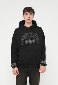 Μαύρο φούτερ με κουκούλα από βαμβακερό μείγμα, με μεγάλο εκτυπωμένο σχέδιο σε λευκό χρώμα μπροστά και διακοσμητικές λεπτομέρειες στα μανίκια.