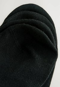 Quatre chaussettes invisibles noires empilées sur un fond clair, montrant la texture tricotée et la forme arrondie des orteils.