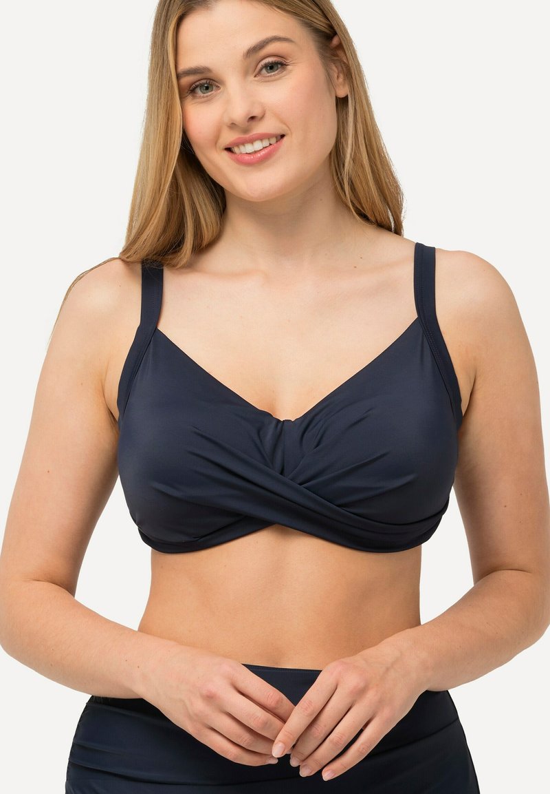 Marineblauwe bikinitop met een gedraaide voorkant, verstelbare bandjes, gecapitonneerde cups en een gladde textuur. Minimalistische stijl met een strakke uitstraling.