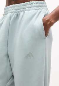 Κοντινό πλάνο ατόμου που φοράει αθλητικές φόρμες Adidas σε ανοιχτό μέντα πράσινο με ελαστική μέση και χέρι στην τσέπη.