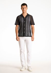 Camisa negra de manga corta con un diseño texturizado de tejido abierto, que presenta un escote con cuello y botones blancos. Combinada con pantalones blancos y zapatillas.