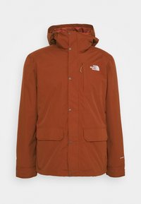 Červená voděodolná bunda s vysokým límcem, zipem a zapínáním na patentky, dvěma předními kapsami a logem na levé horní straně hrudi.