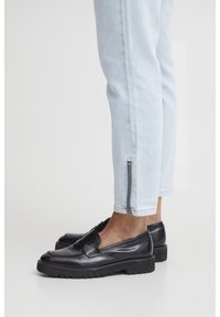 Crne kožne loafers c textured završetkom i blagim petom, uparen sa svijetloplavim tapered hlačama s bočnim zatvaračem na gležnjevima.