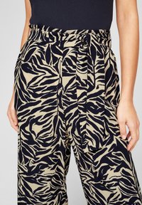 Svart och beige zebramönstrade byxor med hög midja, tygbälte och veckad framdel. Gjorda av lätt material med texturerad design.