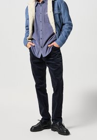 Pánský outfit s džínovou bundou se beránkovým límcem, modrou košilí na knoflíky a tmavými kordurovými kalhotami, doplněný černými lace-up botami.