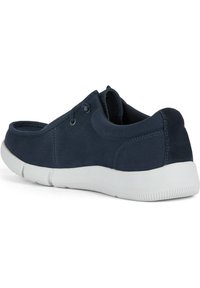 Chaussures en toile bleu marine avec une texture lisse, semelle en caoutchouc blanche et accents élastiques sur les côtés pour un enfilage facile.