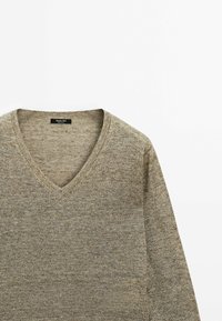 Pull à col en V en tricot texturé de couleur vert olive. Présente un design épuré et minimaliste avec un tissu doux et flexible. Étiquette visible à l'intérieur.