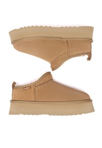 Paar hellbraune Slipper mit dicken Gummisohlen und Zuglaschen, mit weichem Textilobermaterial und Everau Markenlabel an der Seite.