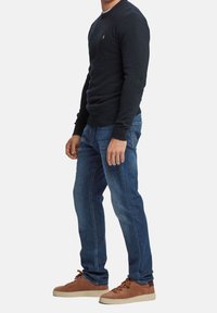 Granatowy sweter z prążkowanymi mankietami, w zestawieniu z niebieskimi dżinsami i brązowymi zamszowymi tenisówkami. Sweter zdobi małe haftowane logo na piersi.