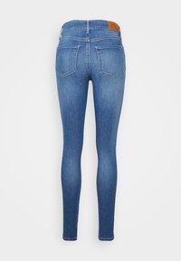 Jeans de denim azul ajustados, con una cintura de altura media, diseño de cinco bolsillos y una etiqueta de cuero marrón en la parte trasera de la cintura.