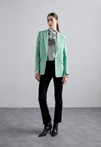 Blazer texturé vert menthe porté sur un haut argent metallique, associé à un pantalon évasé noir et des bottines à bout pointu noires.