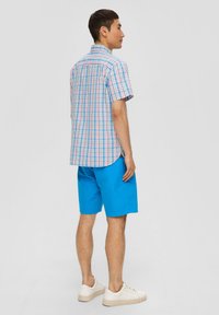 Kurzärmliges karierter Hemd in Pastellblau, Pink und Grün, kombiniert mit einfarbigen blauen Shorts. Lässiges Design mit abgerundetem Saum. Weiße Sneaker.