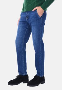 Jeans in denim blu con taglio dritto, cinque tasche, leggeri sbiadimenti e cuciture scure. Abbinati a scarpe stringate in suede nero.