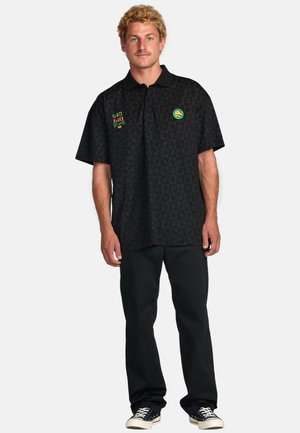 Black short-sleeve polo shirt with a geometric pattern, featuring green, red, and yellow logo accents on the chest. Pair of black pants.