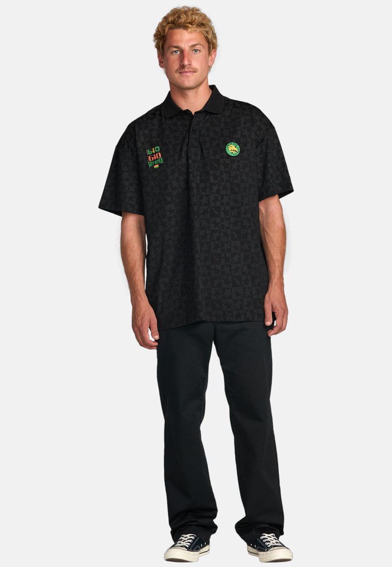 Black short-sleeve polo shirt with a geometric pattern, featuring green, red, and yellow logo accents on the chest. Pair of black pants.