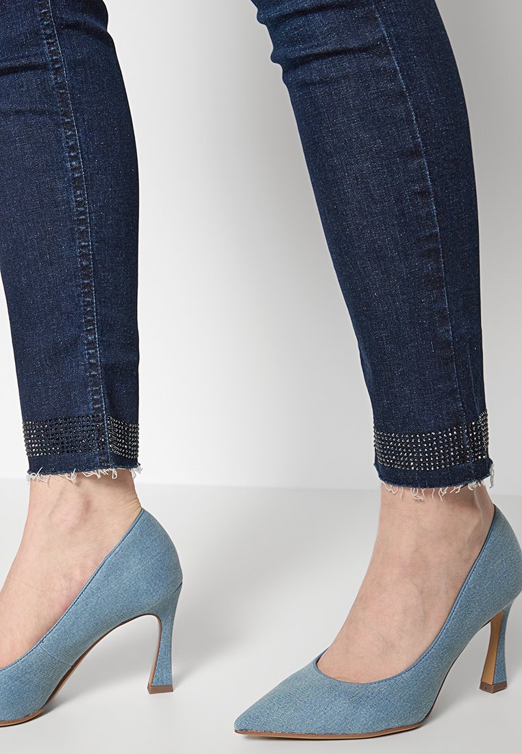 Scarpe con tacco alto in denim azzurro chiaro con punta affusolata. I jeans sono di un blu scuro con risvolti decorati da strass.