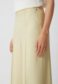 Helle gelbe maßgeschneiderte Hosen mit hoher Taille, seitlichen Nähten, einer glatten Textur und einem kleinen metallischen Akzent in der Nähe der Tasche.