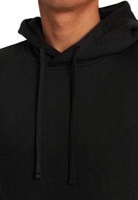 Sweat à capuche noir en tissu texturé, avec un cordon de serrage au cou et une poche kangourou. Vue en gros plan de l'encolure et de la capuche.