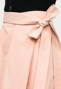 Gonna rosa pallido a vita alta con una larga cintura di stoffa annodata in un fiocco in vita, abbinata a una maglietta nera.