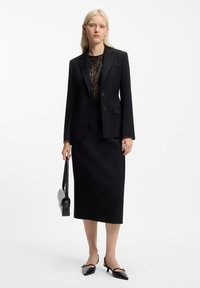 Czarna, dopasowana marynarka na guziki, koronkowa bluzka pod spodem, czarna ołówkowa spódnica, pasująca torebka oraz szpilki z ozdobnymi akcentami.
