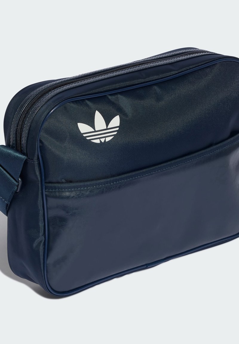 Synthetische Tasche in Marineblau mit glatter Textur, Reißverschlussfach und weißem Adidas-Logo. Verfügt über einen verstellbaren Gurt für einfaches Tragen.