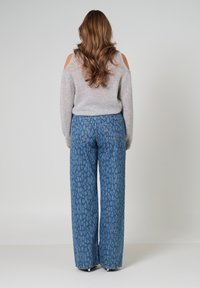 Lichtgrijze, cold-shoulder trui gecombineerd met hoge taille, wijde jeans met een blauw luipaardpatroon. Zachte texturen en een ontspannen pasvorm.