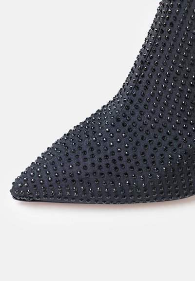 Black stiletto shoe with a pointed toe, covered in small black studs on a textured fabric. Design features a slim silhouette.