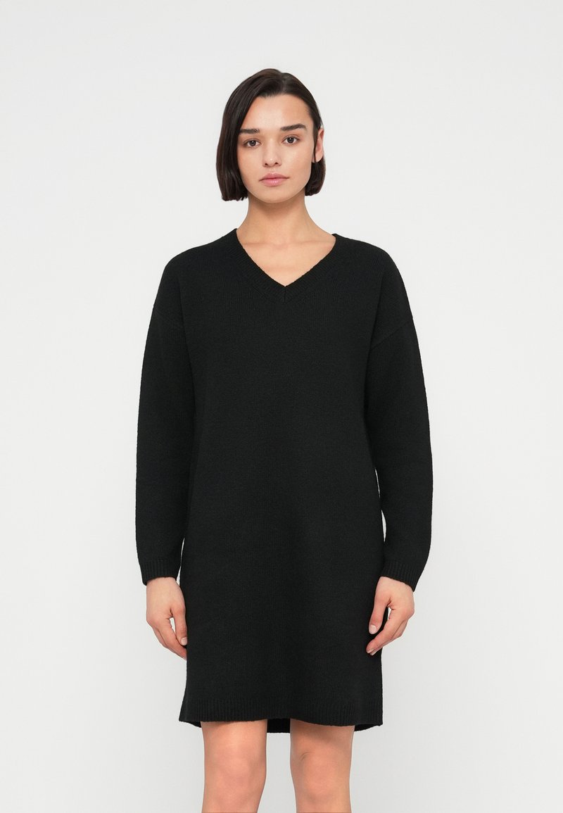 Μαύρο πλεκτό φόρεμα με V-λαιμόκοψη, μακριά μανίκια και άνετη γραμμή. Διαθέτει ριμπ μανσέτες και μήκος μέχρι το μέσο του μηρού. Ορατή απαλή υφή.