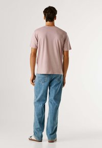 Svetlo roza kratkoročni majica s kratkimi rokavi in okroglo izrezom, kombinirana z ohlapnimi modrimi jeans hlačami z zadnjimi žepi.