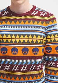 Bunt gestrickter Pullover mit geometrischen und Totenkopfmustern in Orange, Weinrot, Gelb, Blau und Schwarz, mit rundem Ausschnitt.