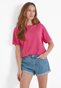 Fuchsia cotton t-shirt with short sleeves, relaxed fit, round neckline, paired with light blue denim shorts, cuffs turned up.