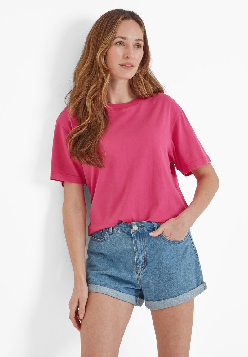 Fuchsia cotton t-shirt with short sleeves, relaxed fit, round neckline, paired with light blue denim shorts, cuffs turned up.