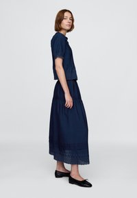 Conjunto azul marino de dos piezas que incluye un top de manga corta con borde de ojalillos y una falda larga con volantes y dobladillo bordado. Combinado con zapatos planos negros.