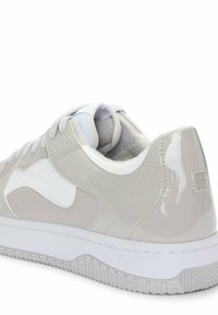 Light gray sneakers featuring a shiny patent finish, white accents, textured laces, and a thick white rubber sole with an embossed logo.