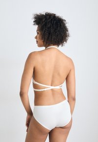 Hvit bikini med halterneck-design, med et kryssryggbånd og glatt, tettsittende bunn. Materialet ser ut til å være elastisk.