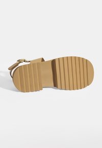 Braune Sandalen mit geriffelter Gummisohle, minimalen Riemen und einer goldfarbenen Schnalle. Flaches Design mit strukturiertem Obermaterial für besseren Halt.