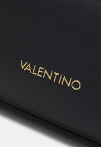 Black leather bag featuring a gold "VALENTINO" logo prominently displayed. Smooth texture with clean lines and minimalistic design.