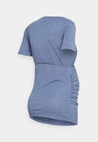 Vista trasera de una blusa de maternidad de manga corta en azul brezo, con fruncido lateral y lazo ajustable en la cintura.