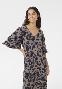 Rochie cu imprimeuri în taupe șters, cu modele abstracte de culoare albastru închis. Prezintă decolteu în v, mâneci scurte tip puff și o croială lejeră. Material cu textură moale.