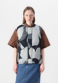 Svart och vit blommönstrad väst med rundad halsringning över en brun kortärmad skorta, tillsammans med en blå denimkjol.