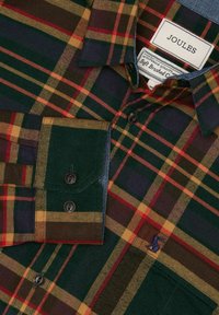 Tumši zaļš, sarkans un sinepju dzeltenais tartāns ar pogām, melnām pogām un apkakli, kā arī Joules zīmola etiķete iekšpusē kakla izgriezumā.