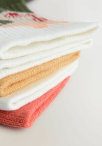 Kolorowa stos czterech złożonych dzianinowych szalików: biały, jasny żółty, beżowy i koralowy. Teksturowana tkanina z widocznymi detalami szwów.