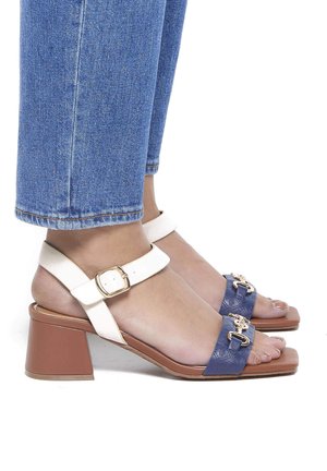 Zweifarbige Absatzsandalen mit einem blauen strukturierten Riemen mit goldenen Beschlägen und einem weißen Knöchelriemen, quadrater Zeh und einem braunen Blockabsatz.