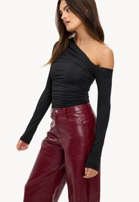 Zwarte one-shoulder top met gerimpeld ontwerp, gecombineerd met bordeauxrode broek in faux-krokodillenstructuur met wijde pijpen. Lange mouwen, aansluitende silhouet.