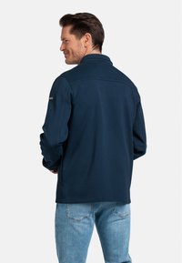 Navyblauwe fleecejas met een subtiele kraag, lange mouwen en een soepele textuur. Beschikt over een minimalistisch ontwerp en een logo op de linkerschouder.