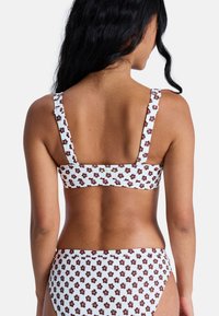 White bikini top with brown floral pattern, adjustable straps, and a small green logo. Smooth texture and fitted design.