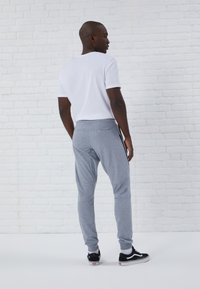 Gray joggers with side stripes and elastic cuffs, paired with a plain white t-shirt. Smooth fabric, relaxed fit, and simple design.